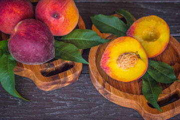 background with peaches above. peaches in wooden bowls and green leaves close-up. whole peaches and half peaches on the table.