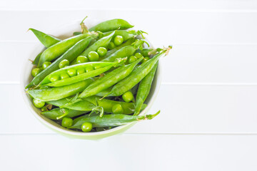 sweet green pea pods in a green bowl on a white background above. green peas and a copy of space. background with green pea pods.