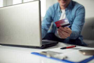 Fototapeta premium Young man using credit card to pay bills online