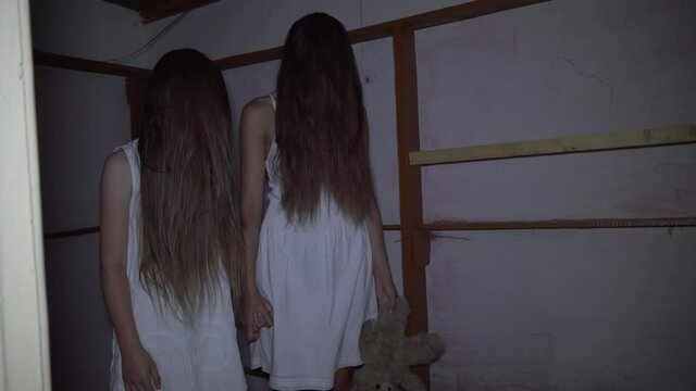 two girls with long black hair and a white dress are standing in an old abandoned room.. The concept of a horror maniac. Halloween. she's holding a Teddy bear,