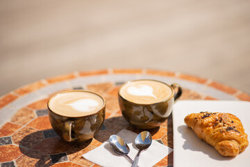 Two cups of cappuccino and a croissant on a cafe table on a bright Sunny day. Space for text at the top. The horizontal frame.