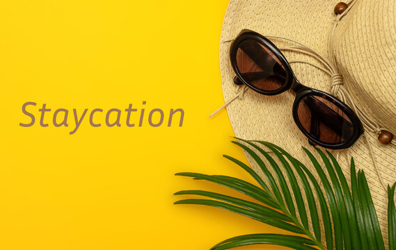 Creative composition on the theme of summer holidays. Hat, glasses and palm branch on a yellow background. Text a STAYCATION. The concept of holiday, vacation, travel