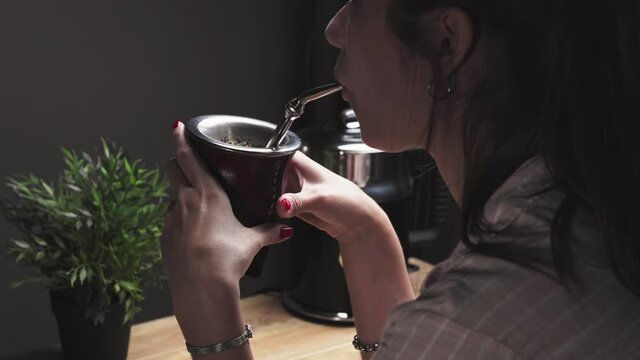 Beautiful young woman drinking Argentinean Mate (Mate Argentino). Traditional infusion beverage common in Argentina, Uruguay, Paraguay  and Brazil. Girl from Argentina holds ad drinks Mate with straw
