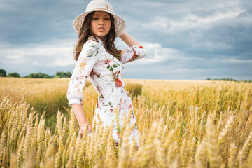 young, emotional, pretty girl in a light dress with a light hat at sunset in a wheat, golden field 