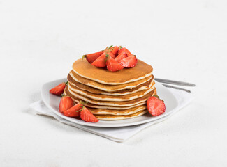 Pancakes with fresh strawberries on a plate on a linen napkin on a white background