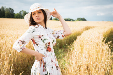 portrait of a young, emotional, beautiful girl in a light dress with a light hat at sunset in a wheat, gold field