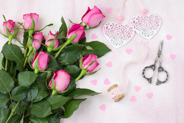 on a pink background a bouquet of pink roses, lace, confetti, scissors and two hearts