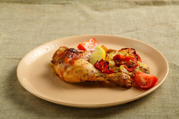 Baked chicken leg with potatoes and tomato on a beige plate on a linen tablecloth.