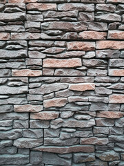 The texture of narrow flat stones in gray-brown tones. Abstract stone wall background for designers. Wall of brown embossed decorative brick. Front view.