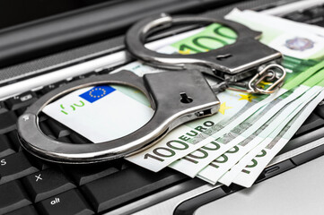 Euro bills and handcuffs on laptop keyboard. Cyber crime.