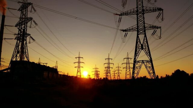 Transmission towers at orange sunset. Electricity pylons. Moving through electric high voltage pylon against the setting sun. Energy efficiency conception.