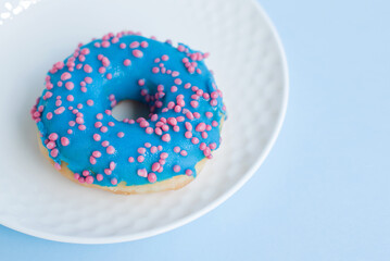 Close-up view of bright colorful donut on a small white plate with blue background. Fresh sweet...