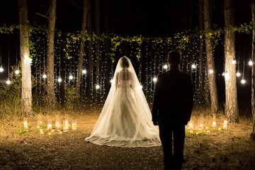 Wedding ceremony night. Meeting of the newlyweds, the bride and groom in the coniferous pine forest of candles and light bulbs.