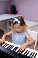 a charming six year old blonde girl in a blue dress plays the piano in her bedroom