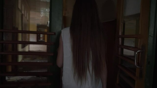 a girl with long black hair and a white dress is walking slowly in a dark corridor. The concept of a horror maniac. Halloween. she is holding a Teddy bear,