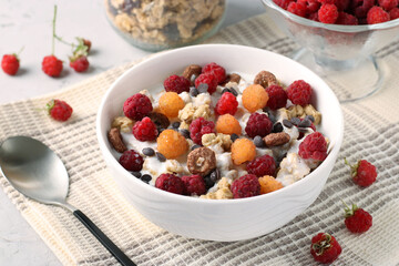 Granola crispy honey muesli with natural yogurt, fresh red and yellow raspberries, chocolate and nuts in a bowl on gray background, healthy food, close up