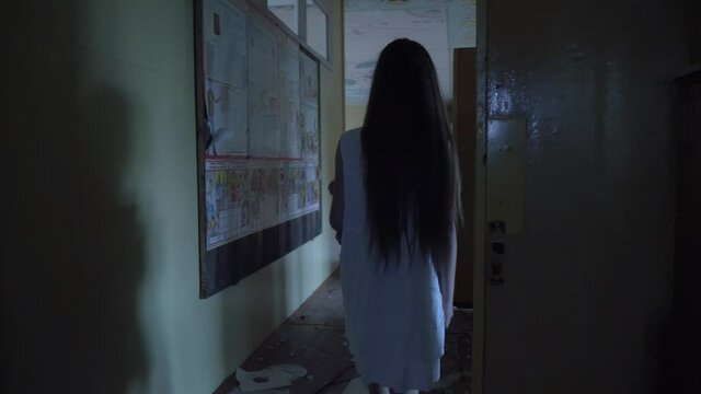 a girl with long black hair and a white dress is walking slowly in a dark corridor. The concept of a horror maniac. Halloween. she is holding a Teddy bear,