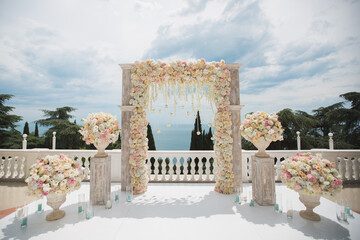 Elegant wedding arch with fresh flowers, vases on background of ocean and blue sky.