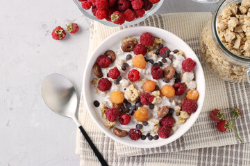 Granola crispy honey muesli with natural yogurt, fresh red and yellow raspberries, chocolate and nuts in a bowl on gray background, healthy food, View from above