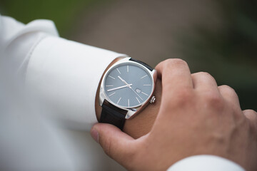 Close up of businessman looking at watch on his hand outdoors, free space. Man in white shirt...