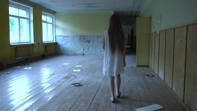 a girl with long black hair and a white dress is walking slowly in a dark corridor. The concept of a horror maniac. Halloween. she is holding a Teddy bear,
