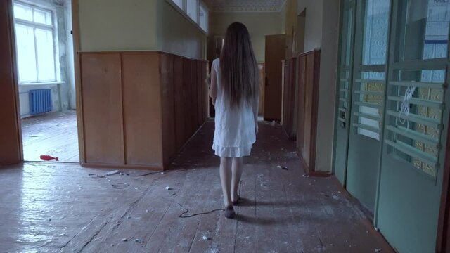 a girl with long black hair and a white dress is walking slowly in a dark corridor. The concept of a horror maniac. Halloween. she is holding a Teddy bear,