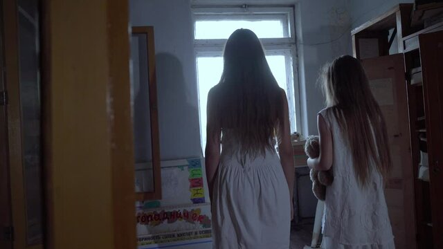 two girls with long black hair and a white dress are standing in the audience of an old abandoned school or house. the concept of maniac terror. Halloween.