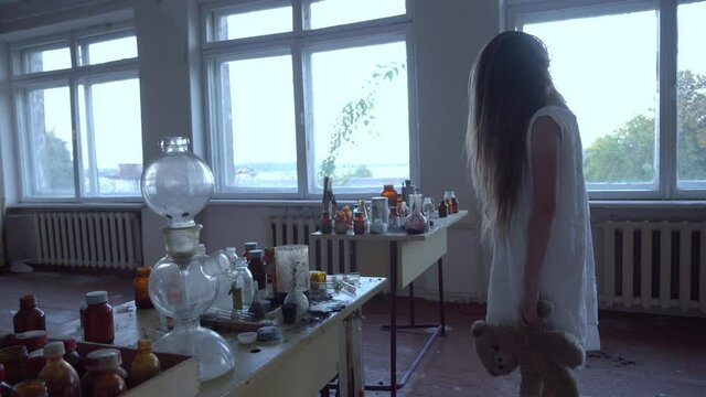 a girl with long black hair and a white dress walks slowly through the dark classroom of the school. The study of chemistry. Against the background of old test tubes and a blackboard.