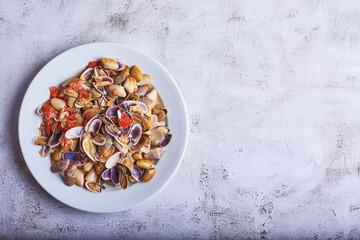 Clams cooked with tomato and onion on a white plate and one of them in the foreground