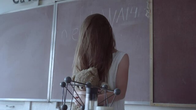 a girl with long black hair and a white dress walks slowly through the dark classroom of the school. The study of chemistry. Against the background of old test tubes and a blackboard.