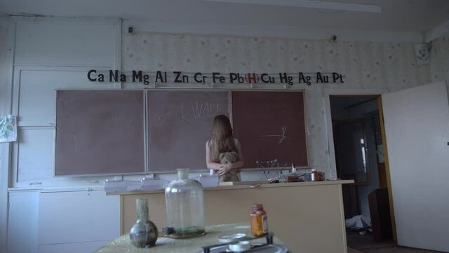 a girl with long black hair and a white dress walks slowly through the dark classroom of the school. The study of chemistry. Against the background of old test tubes and a blackboard.