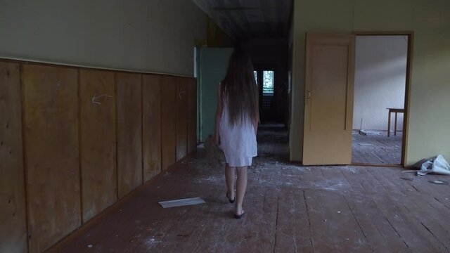 a girl with long black hair and a white dress is walking slowly in a dark corridor. The concept of a horror maniac. Halloween. she is holding a Teddy bear,