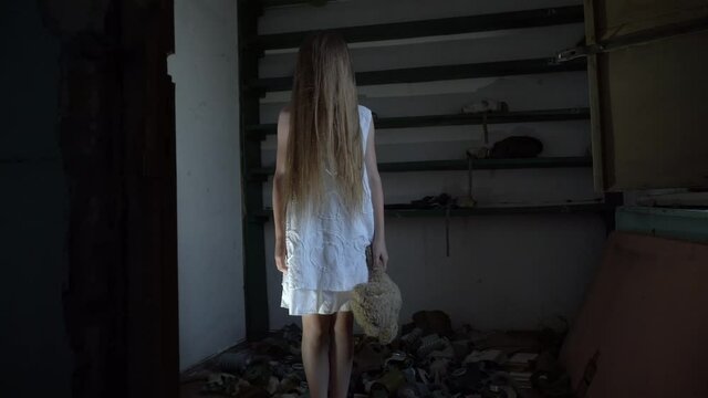 a girl with long black hair and a white dress is walking slowly in a dark corridor. The concept of a horror maniac. Halloween. she is holding a Teddy bear,