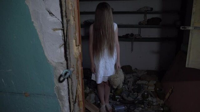 a girl with long black hair and a white dress is walking slowly in a dark corridor. The concept of a horror maniac. Halloween. she is holding a Teddy bear,