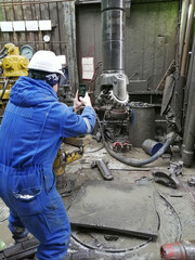A drill bit specialist examines the condition of a bit pulled out of an oil and gas well. The engineer is wearing a blue overalls and a white hard hat.