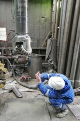 A drill bit specialist examines the condition of a bit pulled out of an oil and gas well. The engineer is wearing a blue overalls and a white hard hat.