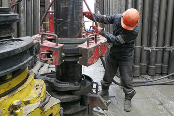 A drilling worker makes up pipes to run the casing into the well with a pneumatic wrench. It is...