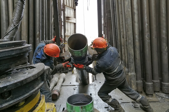 Two drilling crew workers dismantle the bottom of the drill string. Unscrewing the spiral calibrator. Working with a machine key. They are located on the rotary platform of the drilling rig.