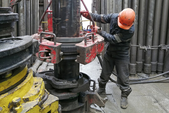 A drilling worker makes up pipes to run the casing into the well with a pneumatic wrench. It is located on the rotary platform of the drilling rig.