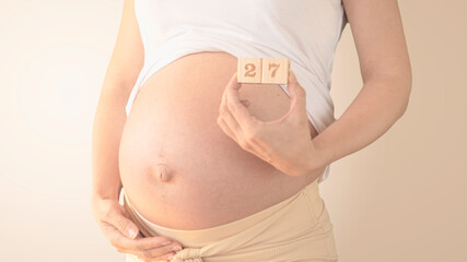 Pregnant young woman with pregnancy week number next to her belly. Photos of belly growth at 27...