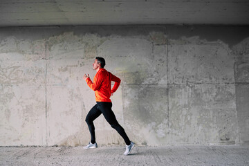 Obraz na płótnie Canvas Full length of middle aged runner running in urban exterior.