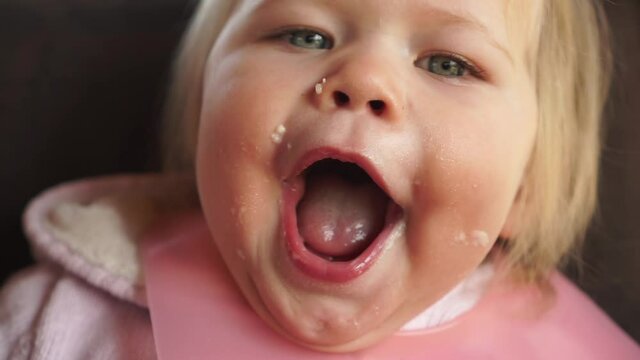 Happy funny chubby baby girl face covered in food mouth wide open hungry waiting for more food positive smiling