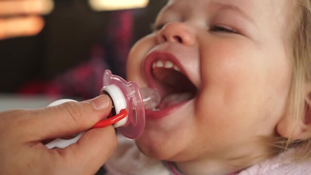 One year old baby girl laugthing playing catching pacifier nipple with her mouth wide open. Children pacifier sucking addiction habbit