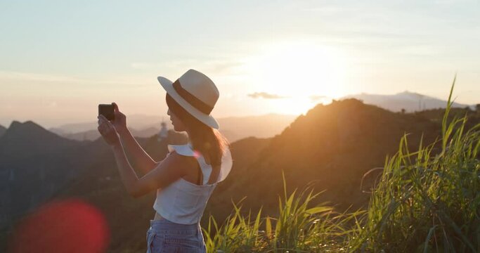 Travel woman wear straw hat and take photo on cellphone look at the mountain view in sunset time