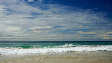 Expansive view from sandy beach across breaking waves to the horizon, under a beautiful blue cloudy sky.  Currumbin Beach, Gold Coast, Queensland, Australia.