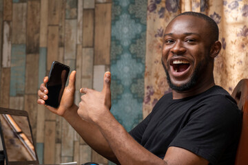 excited young black man holding his mobile phone and pointing to it