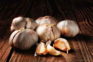 Closeup of a group of Italian garlic cloves on a dark rustic wood table. Light Painting Still Life.