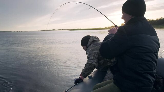 Friends fishing. Two amateur anglers fishing from the boat and fighting with trophy fish