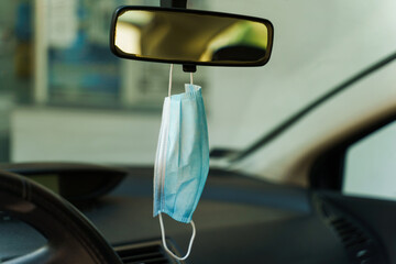 Medical protective face mask in car on the rearview mirror in day - Covid-19 pandemic protection on...