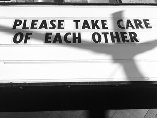 Black and white photo of sign on local business asking the community to take care of each other during coronavirus crisis.  Kindness concept.